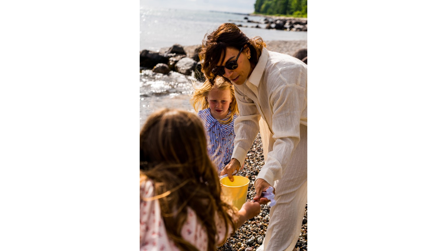 En hyggelig strandscene hvor der leges med gult sandlegetøj mellem sten ved vandkanten.